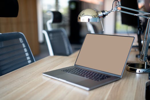 A sleek office setup featuring a laptop on a wooden desk with chairs and a metallic lamp.